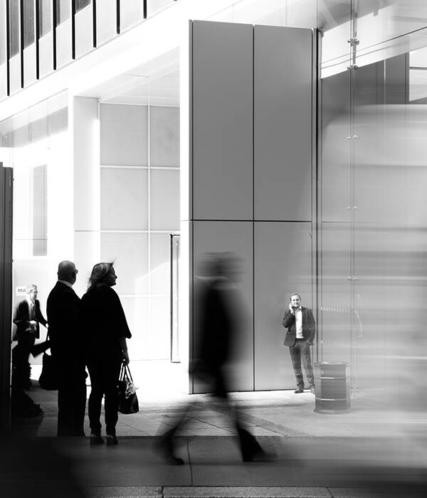 A picture of man on a call in front of building with many people walking around